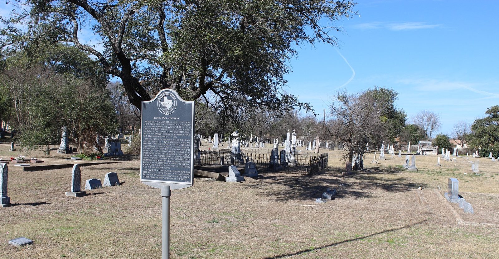Scattered older headstones under an oak tree in a Texas cemetery, daylight
